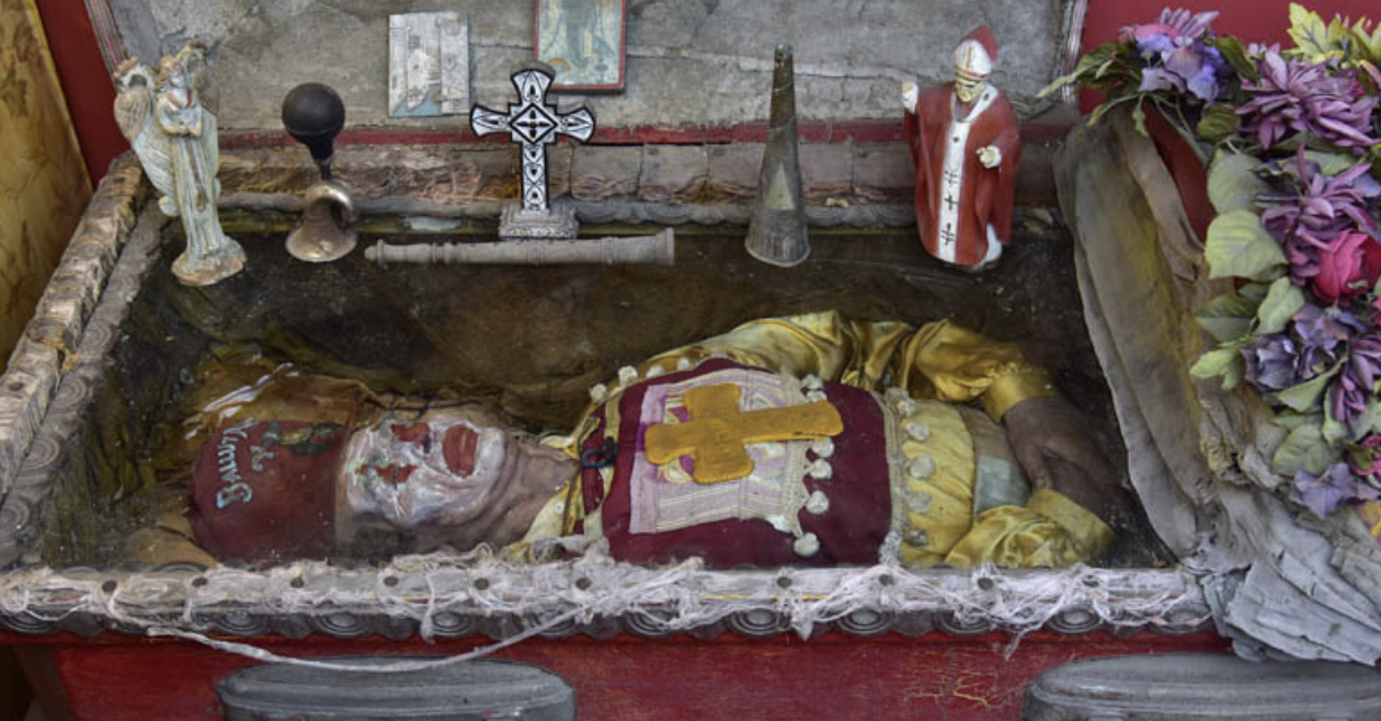 A dead clown in a box surrounded by religious icons and fake flowers. This is how I feel when I think too hard about the clown—like I am trapped inside a box, and the face the world sees is only my makeup.